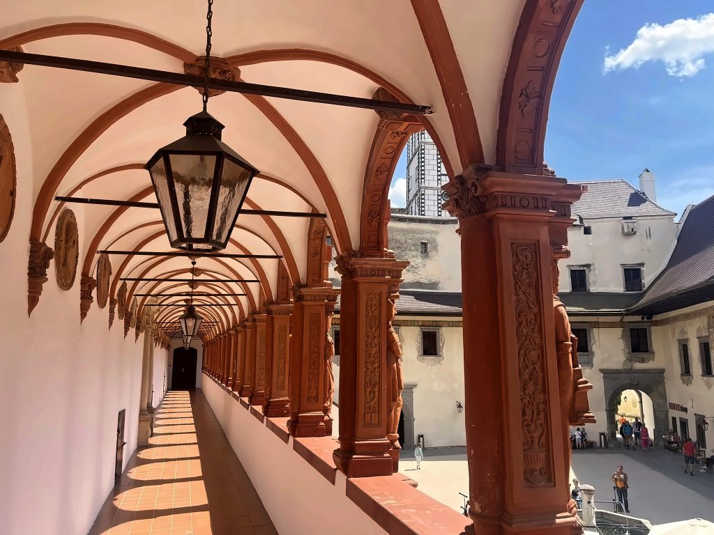 Arkadengang der Renaissance-Schallaburg mit verzierten Terrakotta-Säulen, Gewölbedecke und alter Laterne, Blick in den sonnigen Schlosshof.